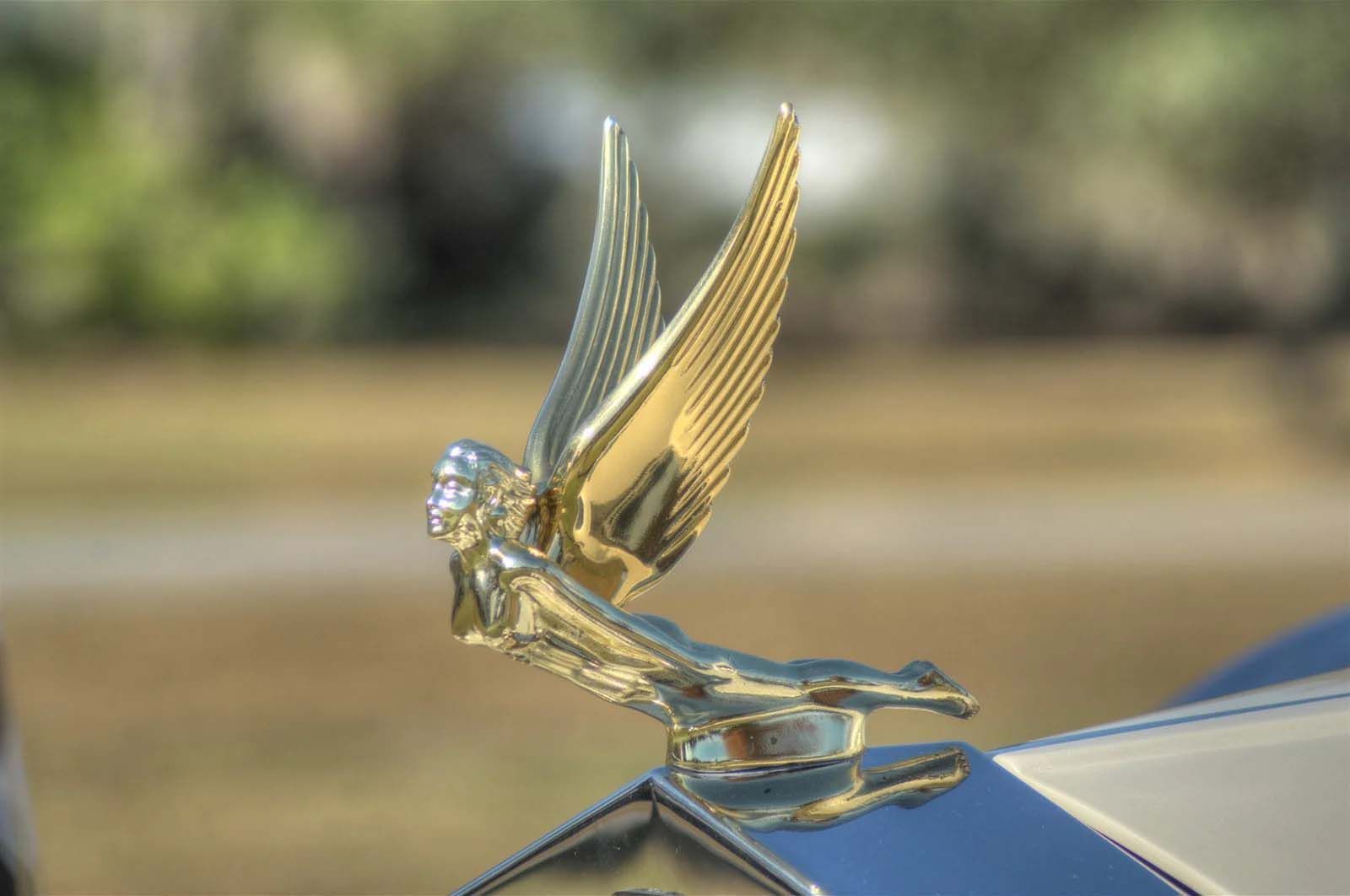 A close up of a car hood ornament with wings on a blue car.