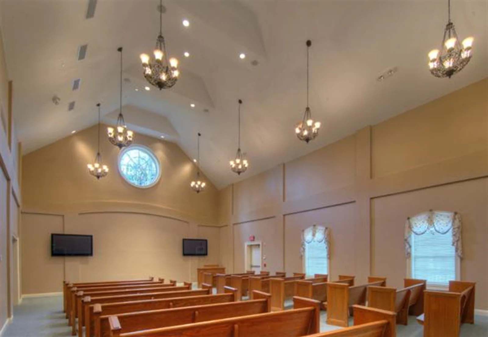 A church with rows of wooden benches and chandeliers hanging from the ceiling