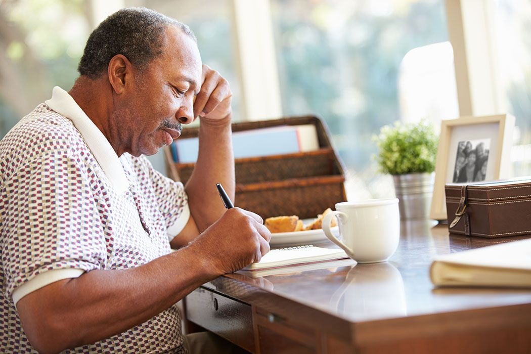 An older man is sitting at a desk writing in a notebook.