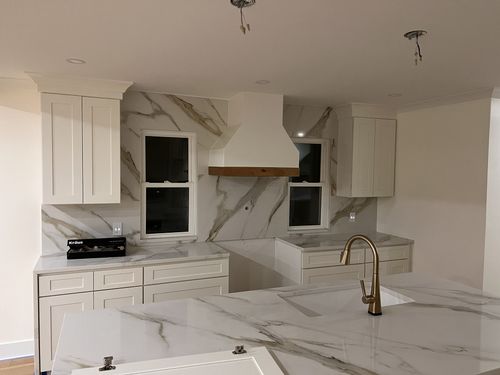 Modern kitchen with white cabinets, marble countertops, and a white range hood.