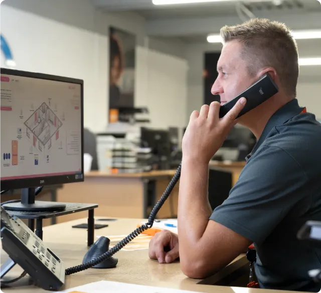Man on phone, looking at a computer screen in an office setting.