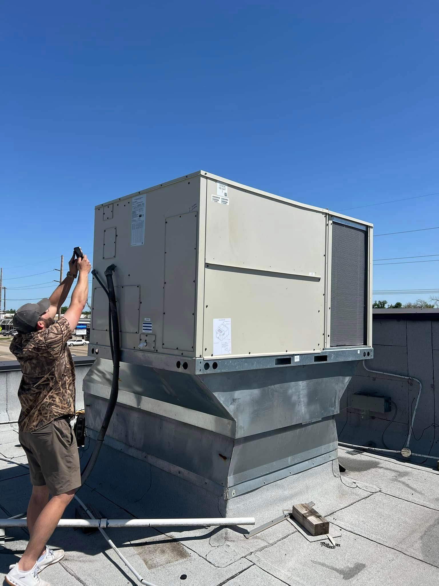 A man is standing next to a large air conditioner on top of a roof.