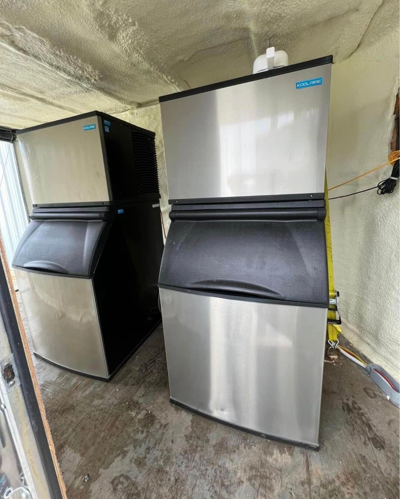 Two stainless steel ice machines are stacked on top of each other in a room.