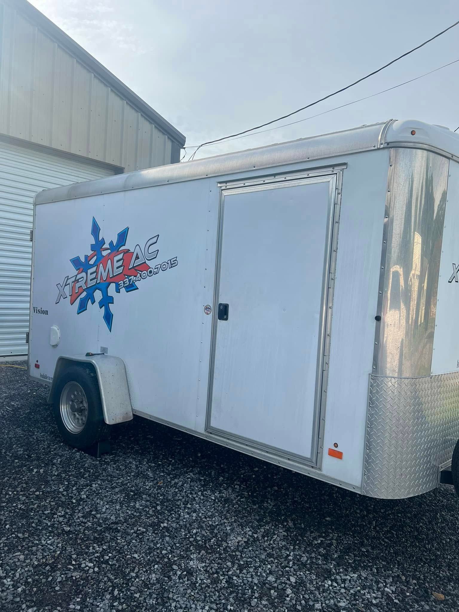 A white trailer is parked in a gravel lot in front of a building.