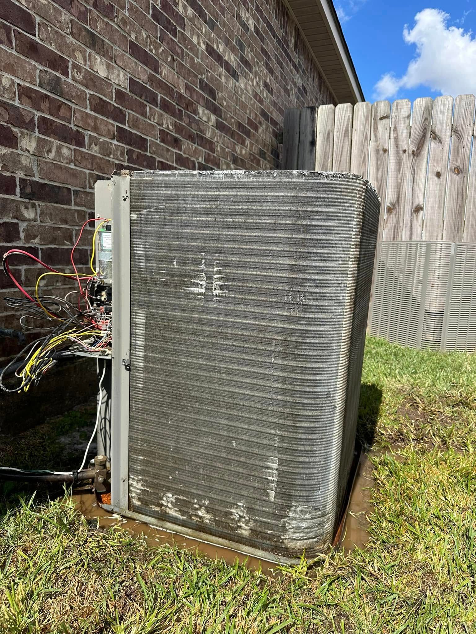 A dirty air conditioner is sitting in the grass in front of a brick building.