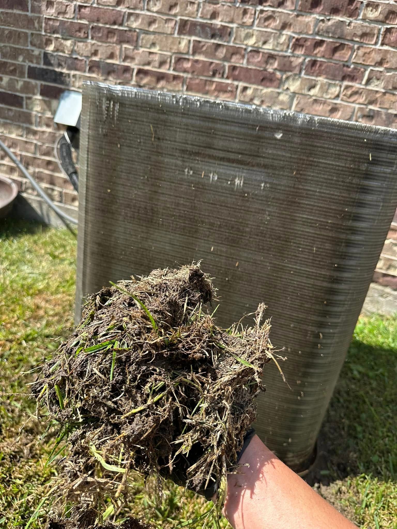 A person is holding a pile of grass in front of a brick wall.