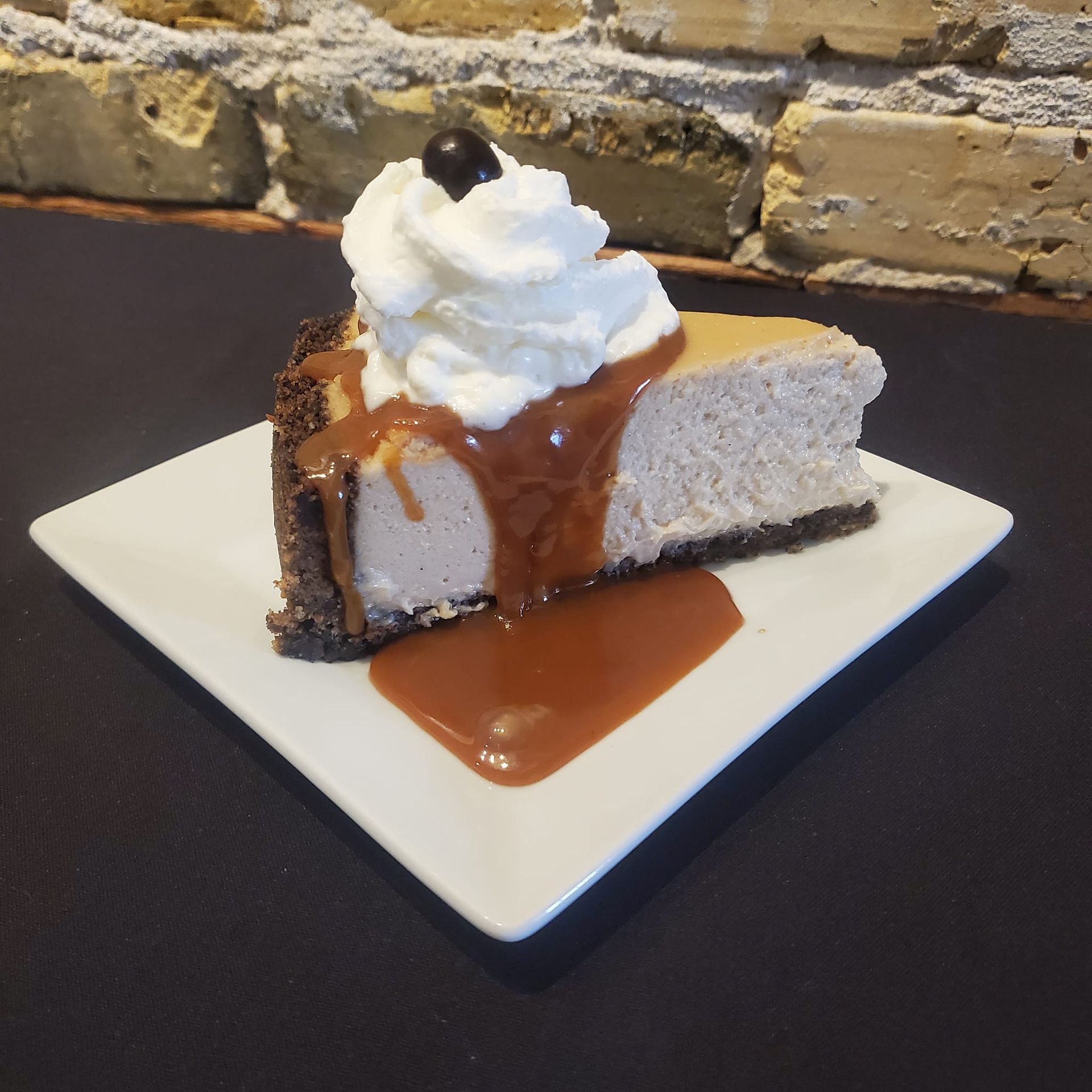 A slice of cheesecake with whipped cream and caramel sauce on a white plate