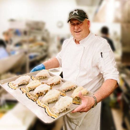 A chef wearing a ny hat is holding a tray of food