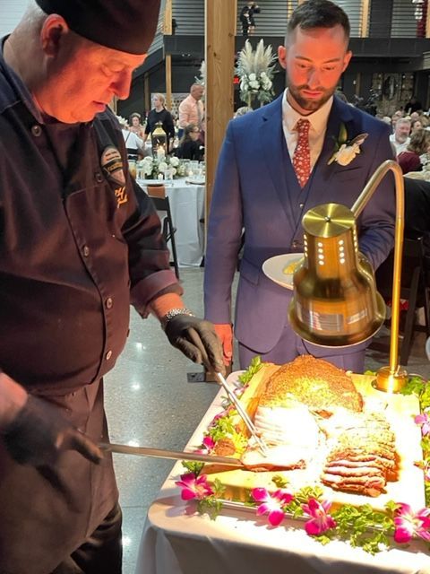 A man in a suit is standing next to a chef cutting food