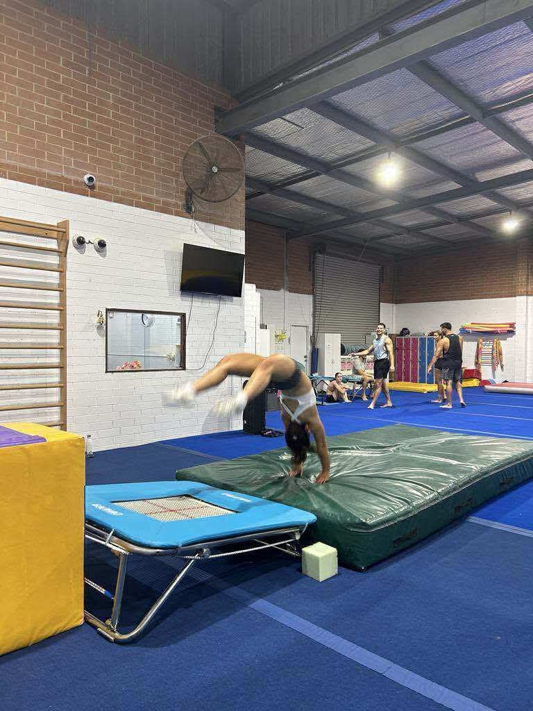 Gymnast in mid-backbend on a mat, transitioning from a small trampoline in a gym.