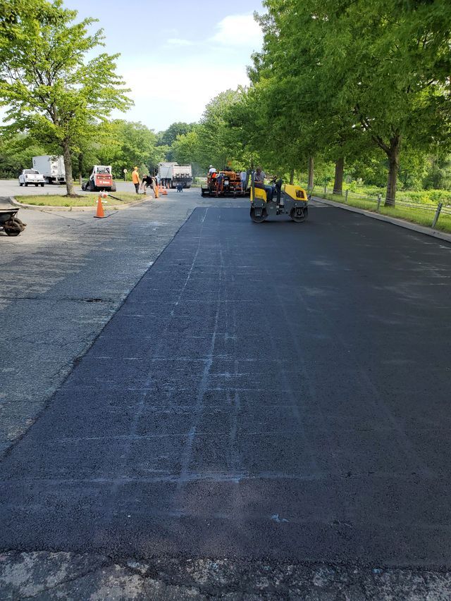A road is being paved in a parking lot with trees in the background.