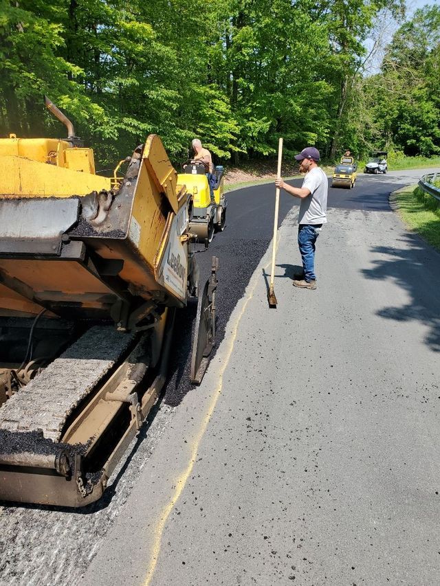 A man with a broom is standing next to an asphalt paving machine