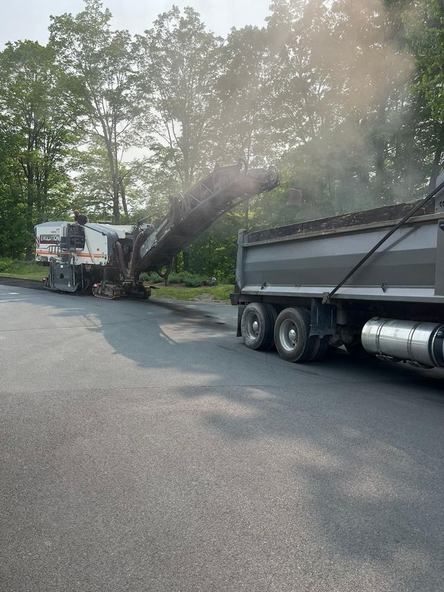 A dump truck is being loaded with asphalt and smoke is coming out of it.