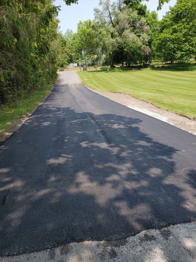 A newly paved road going through a lush green field.