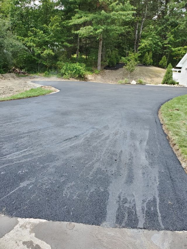 A black asphalt driveway with trees in the background.