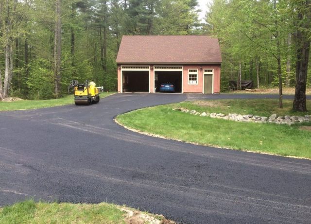 A yellow roller is driving down a road in front of a garage.