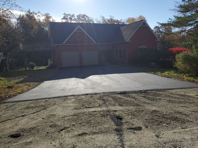 A brick house with a large driveway in front of it.