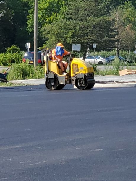 A man is driving a yellow roller on a road.