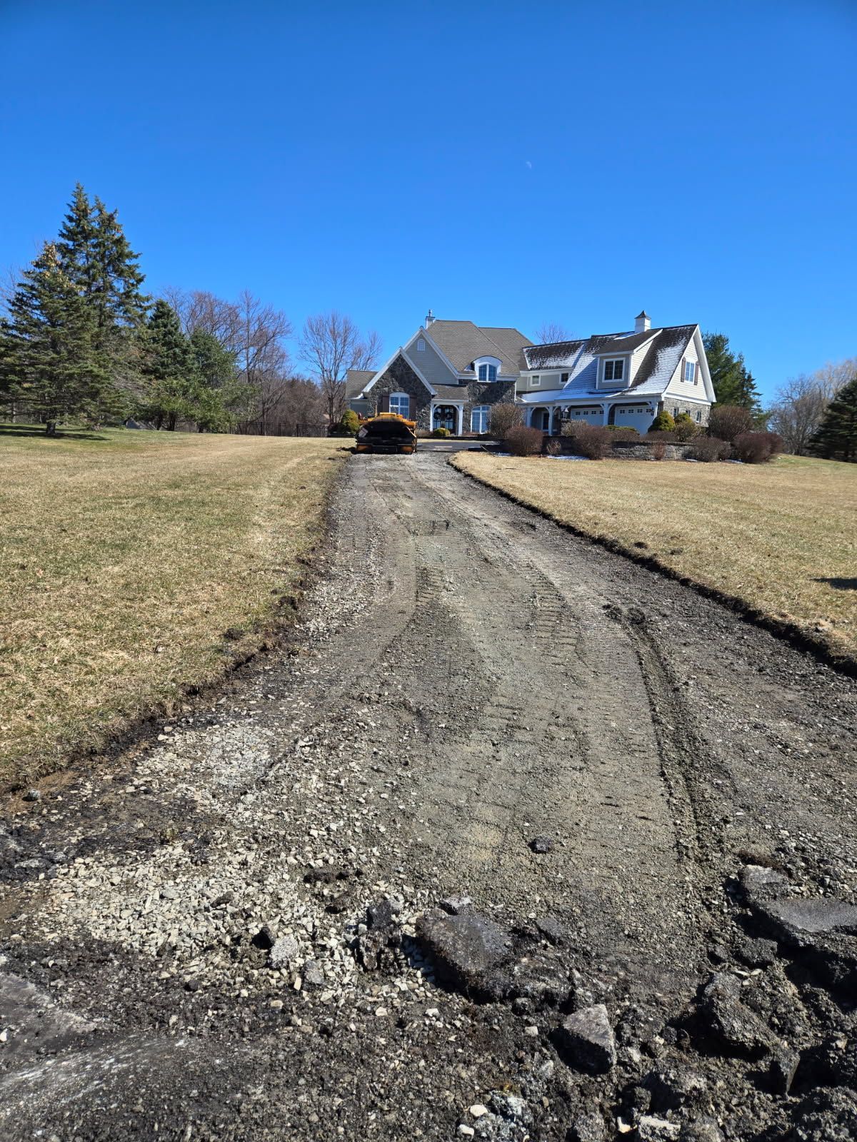A tractor is driving down a dirt road in front of a house.