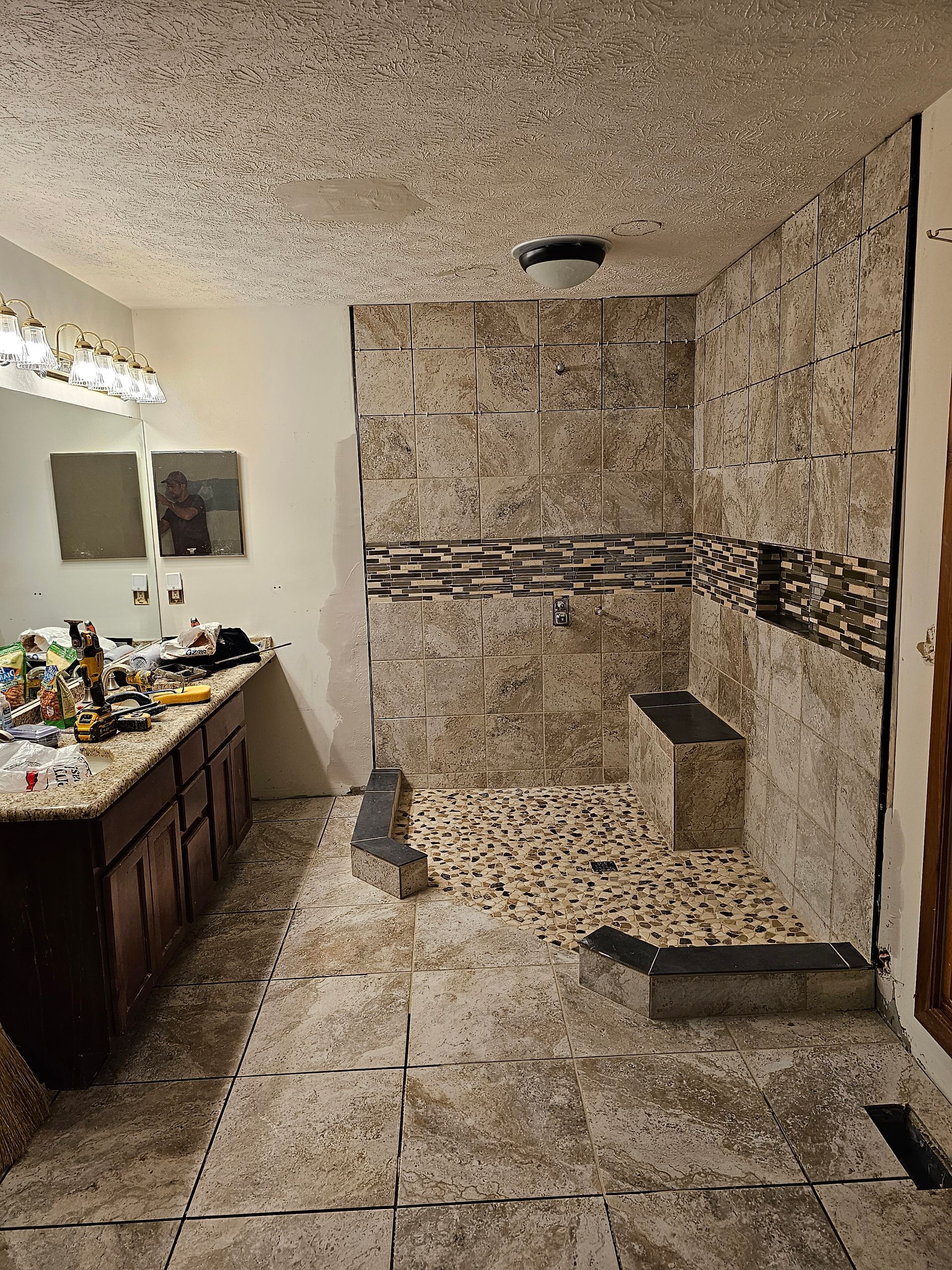 Bathroom under construction with tiled shower, vanity, and brown cabinets.