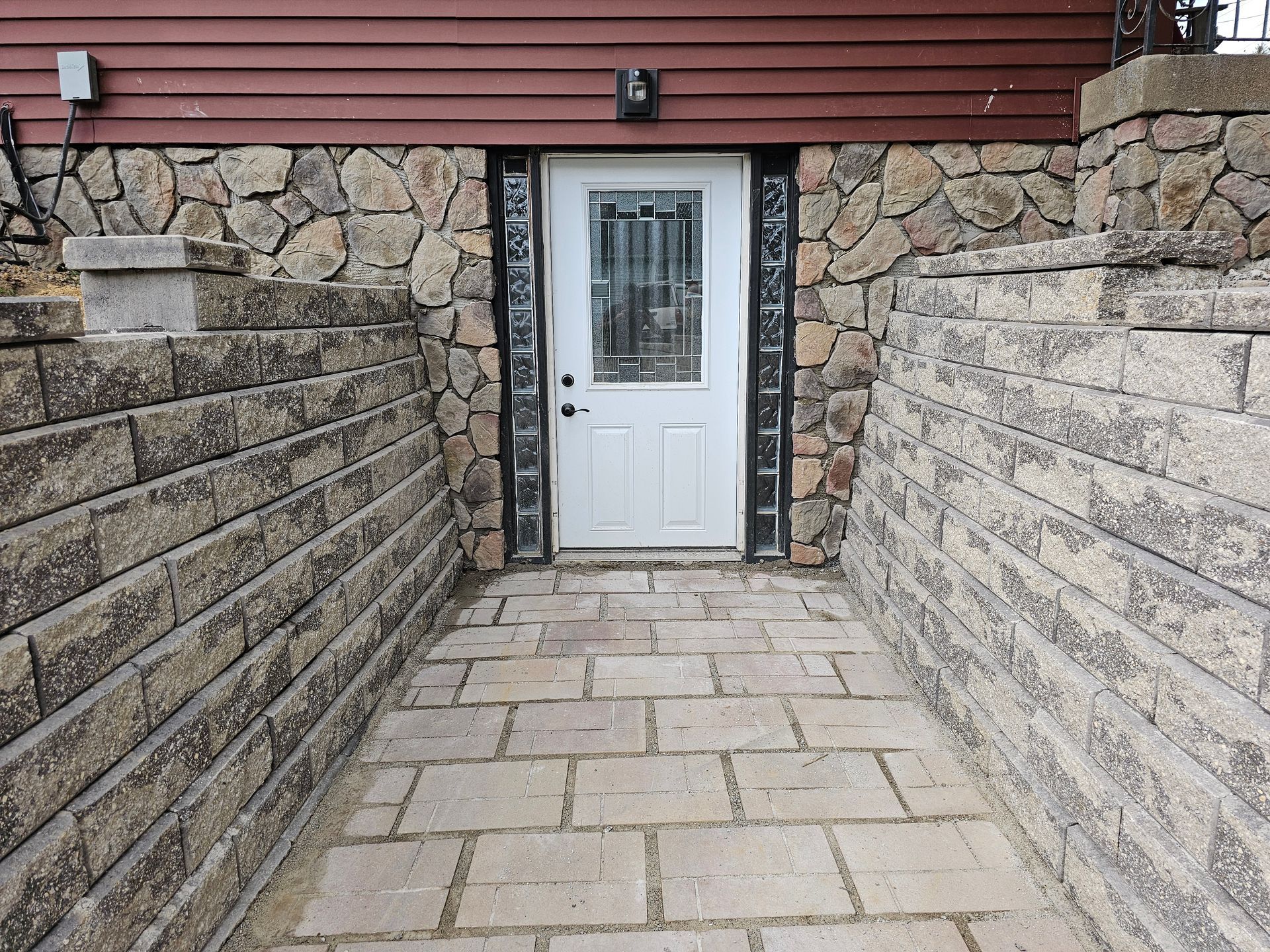 A white door set into a stone and brick alcove.  Leads to a basement entrance.