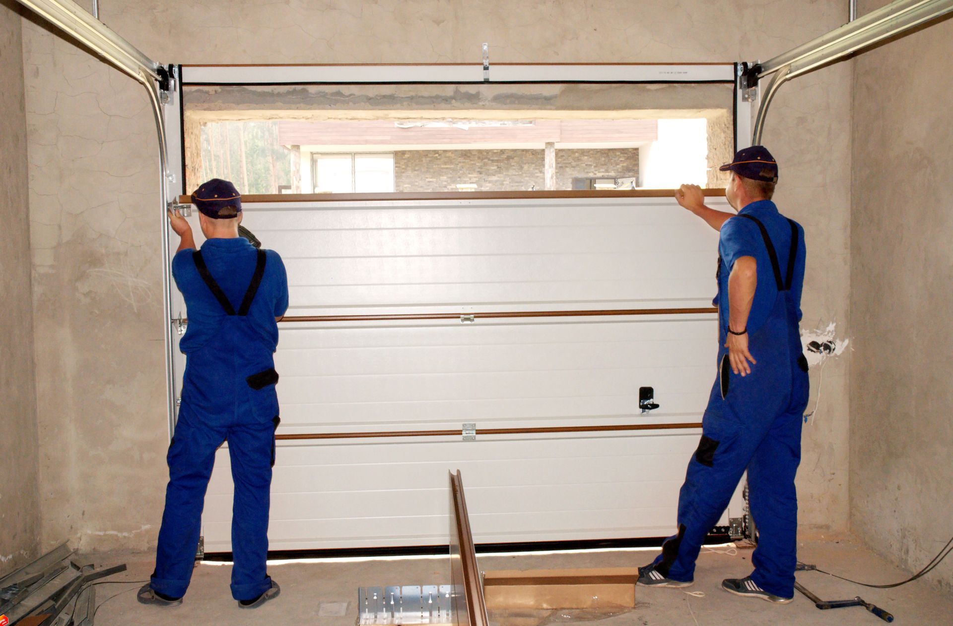 Two installers lifting and aligning a sectional garage door panel inside garage.