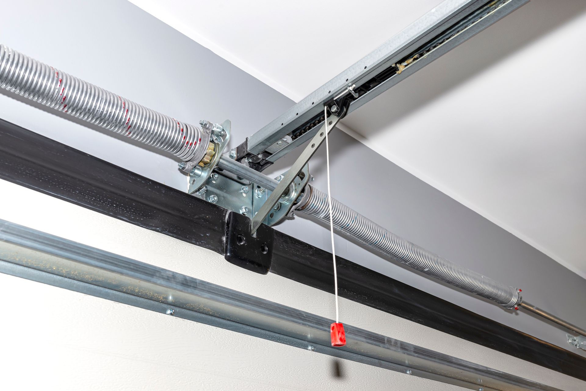 Garage door torsion spring system, silver springs, black track, white ceiling.