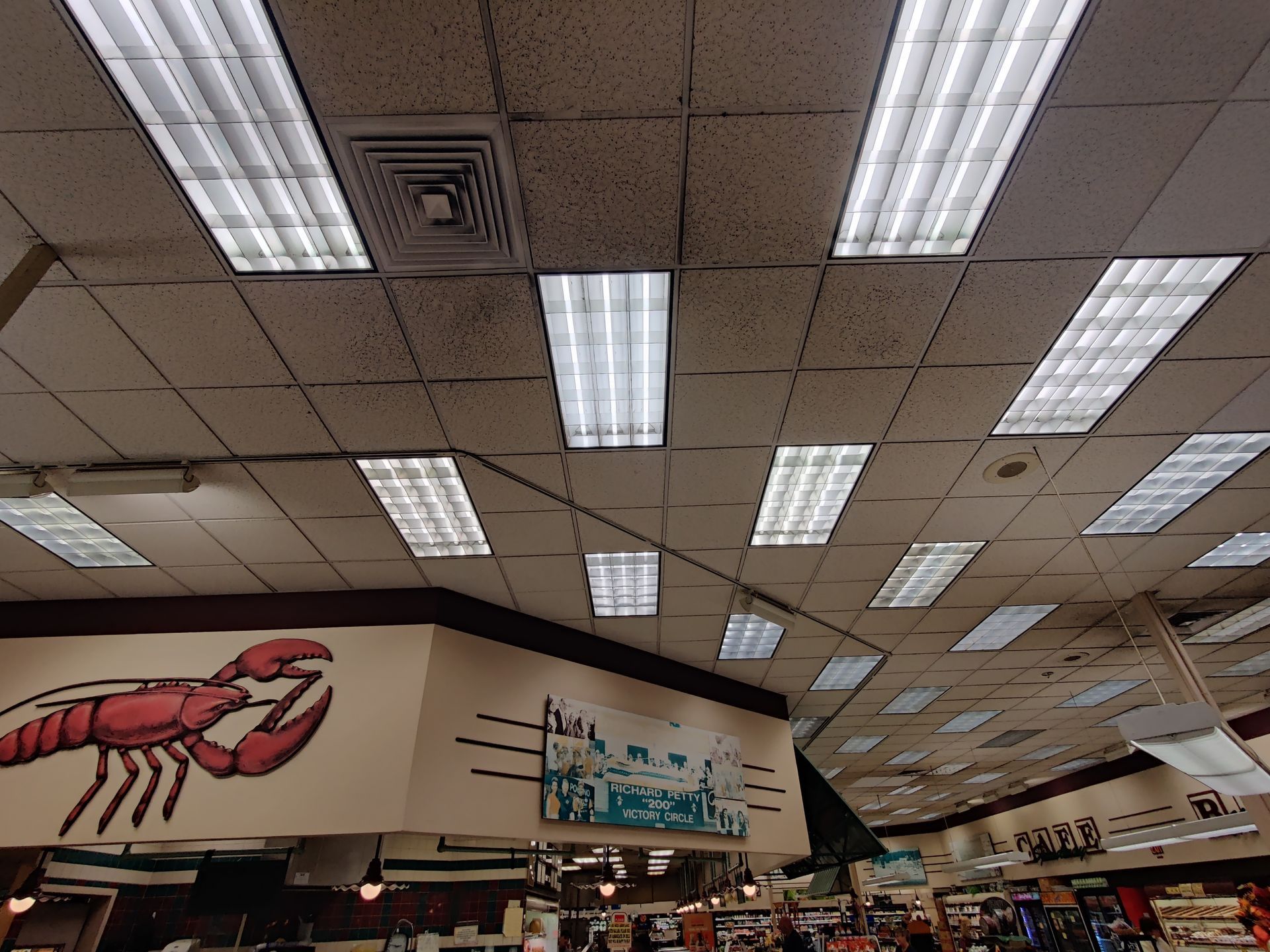 Interior of a grocery store aisle with fluorescent ceiling lights and a large red lobster mural on the wall.