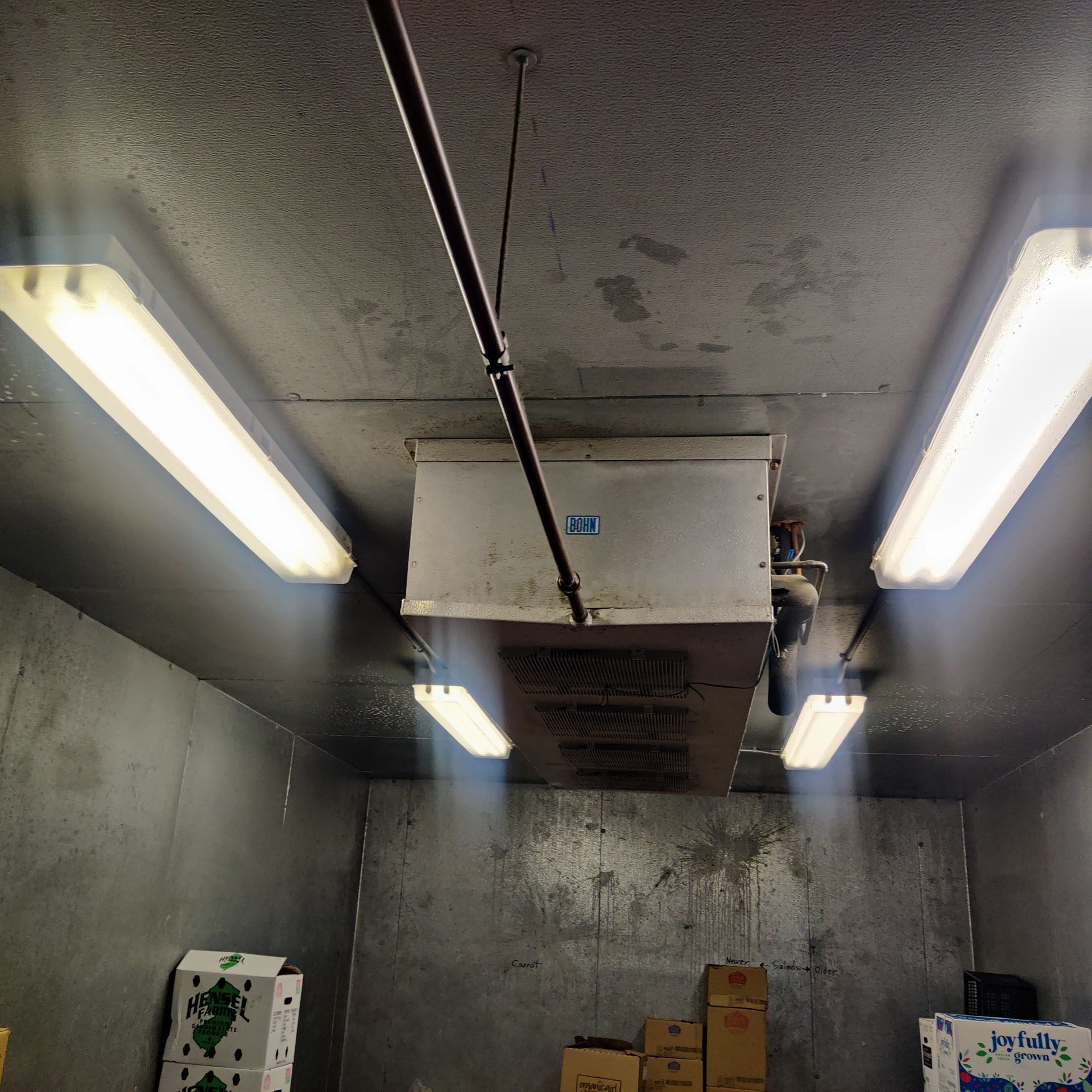 Concrete room ceiling with fluorescent lights and exposed pipes above stacked boxes