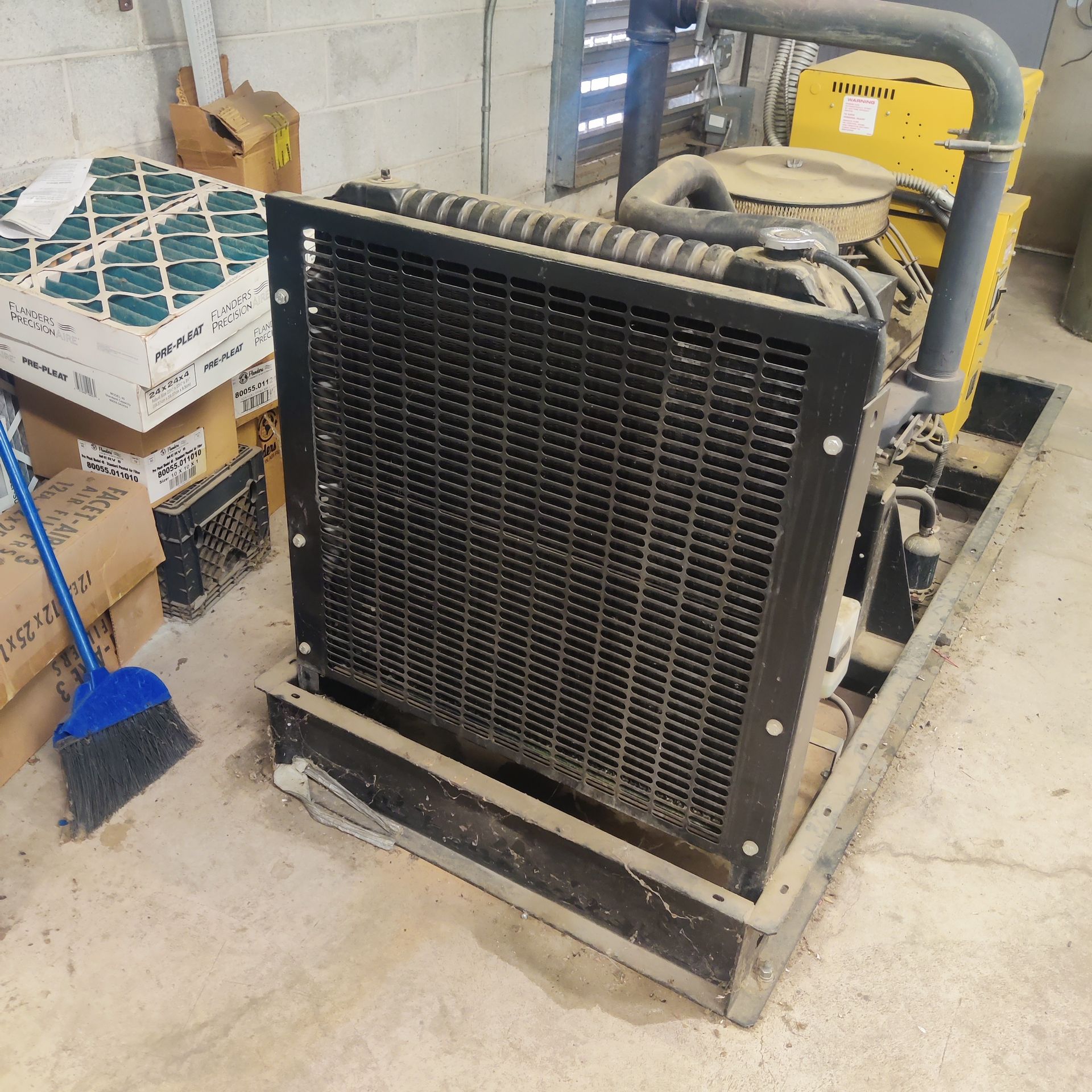 Portable industrial air cooler with black grille beside boxes and a broom in a warehouse.