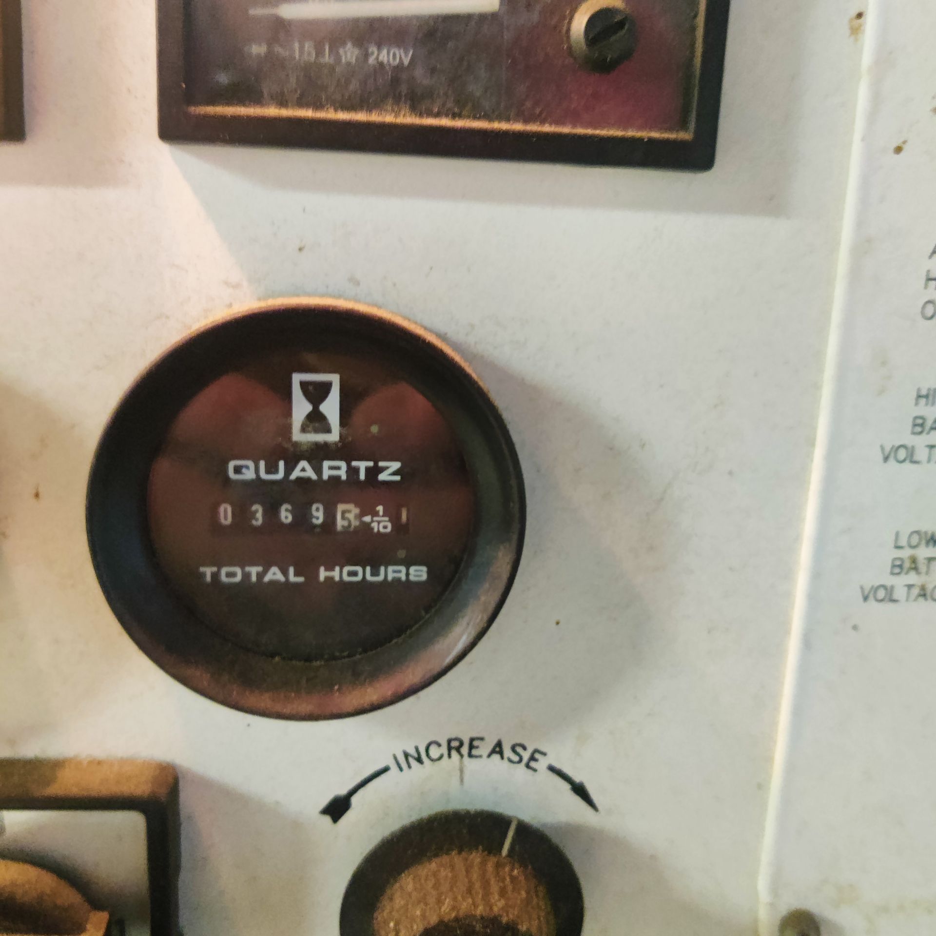 Close-up of a white machine panel with a Quartz total-hours meter and an increase control knob.