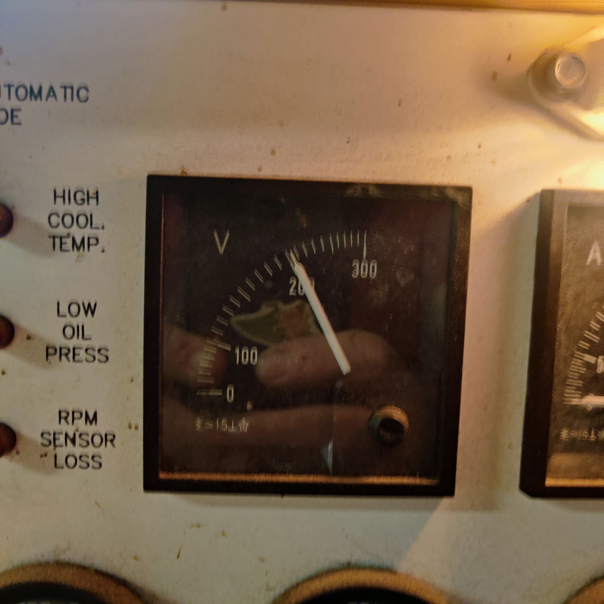Analog gauge on a control panel, showing about 120 volts with warning labels nearby.