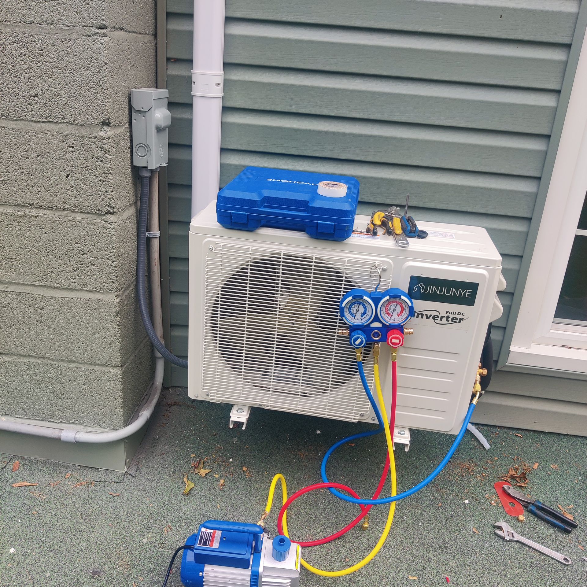 Blue HVAC service gauges attached to a white outdoor air conditioner unit beside a wall