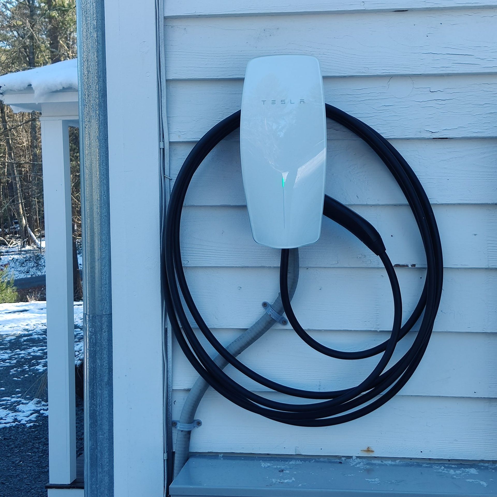 White EV charger mounted on an exterior house wall with a coiled black cable wrapped around it.