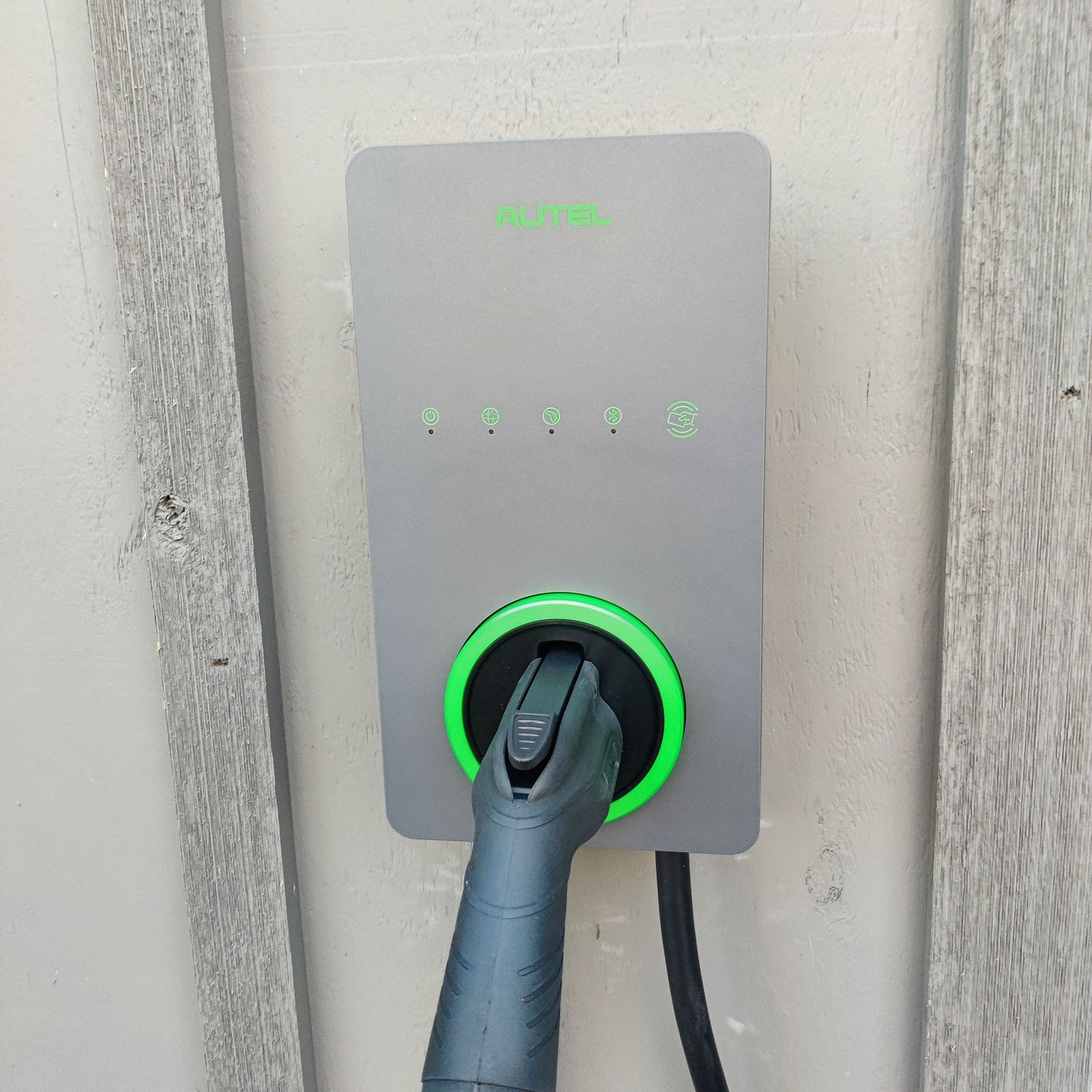Electric vehicle charging station with a plug inserted and a glowing green ring indicator.