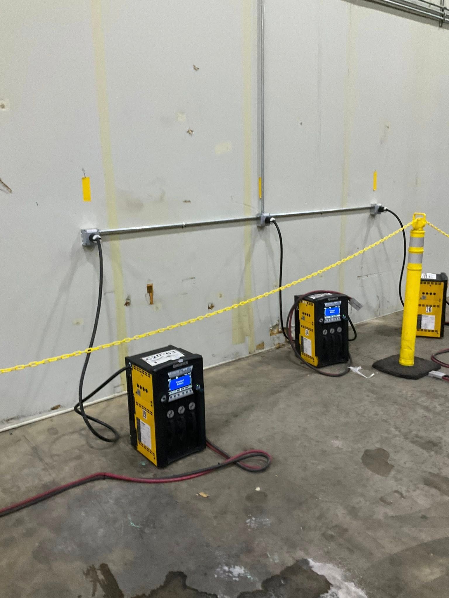 Two welding machines on a concrete floor beside a wall, with cables and a yellow caution tape barrier.