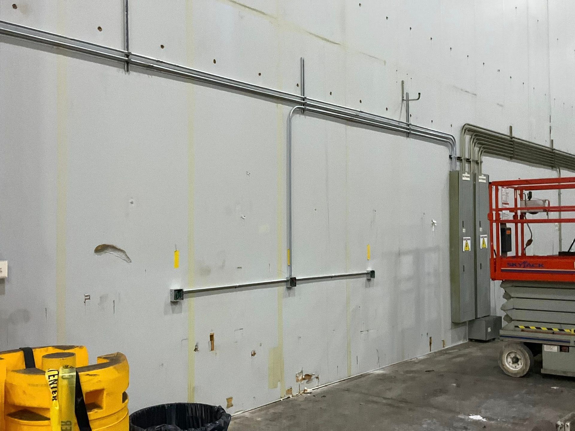 Industrial warehouse wall with conduit, yellow drums, and a red lift near the right side