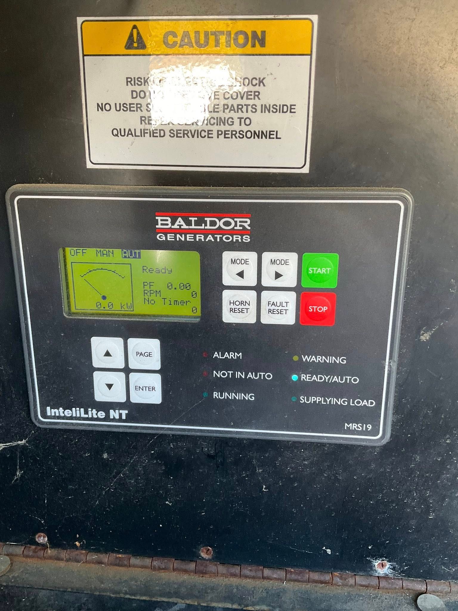 Close-up of a machine control panel with green display, buttons, and a yellow caution label above.