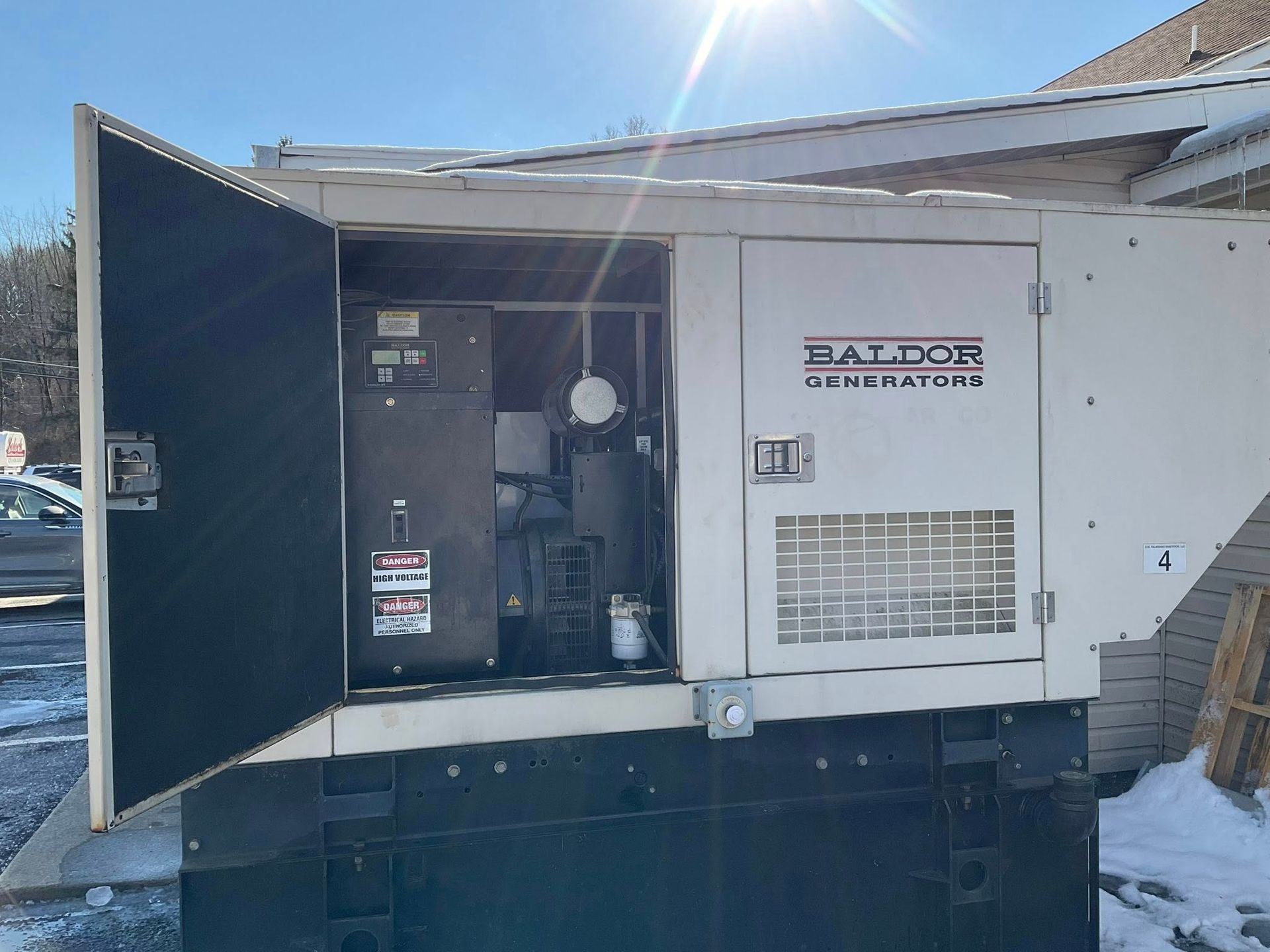 White industrial generator unit in a snowy outdoor service area with open access door.