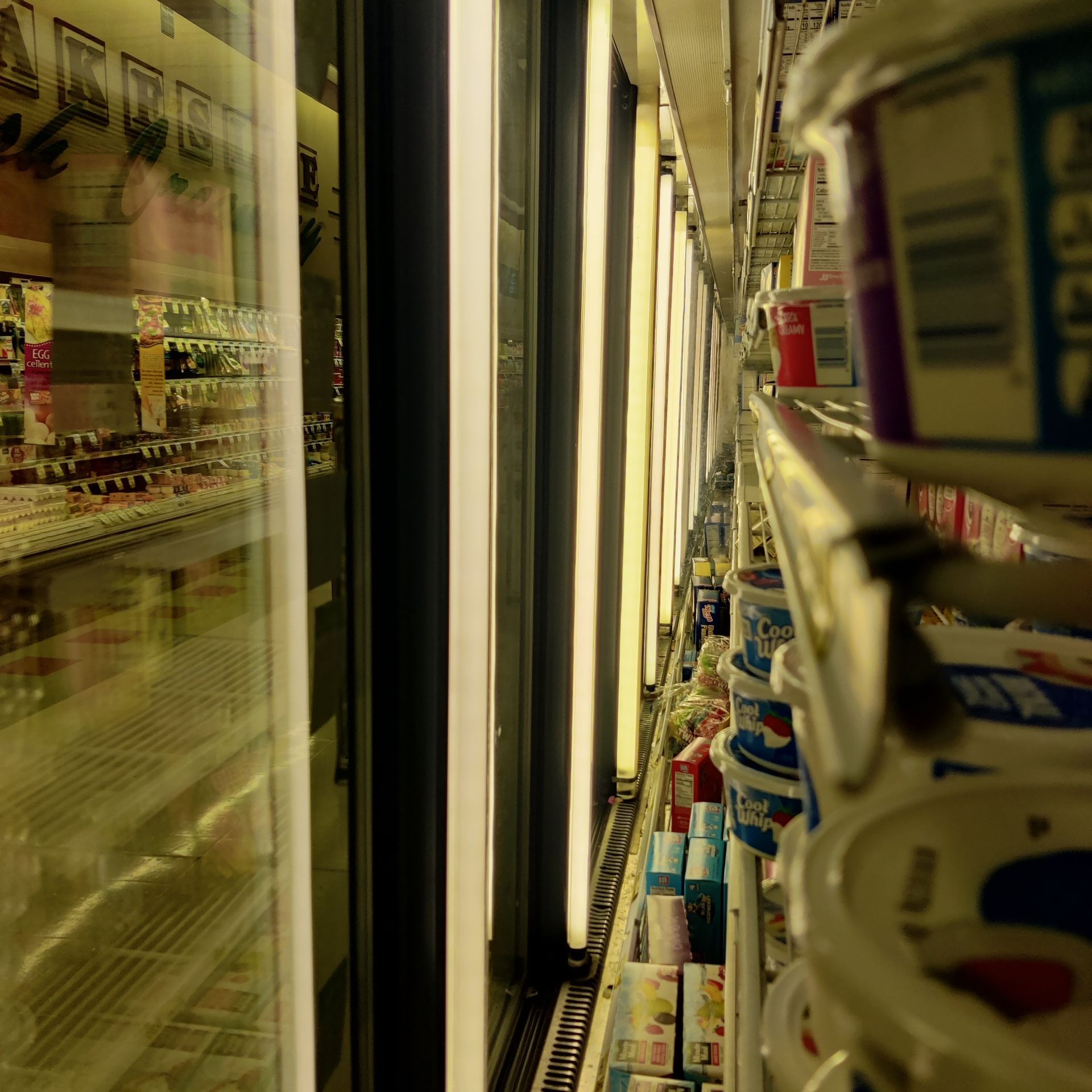 Narrow grocery aisle with refrigerated shelves and rows of packaged drinks and dairy products