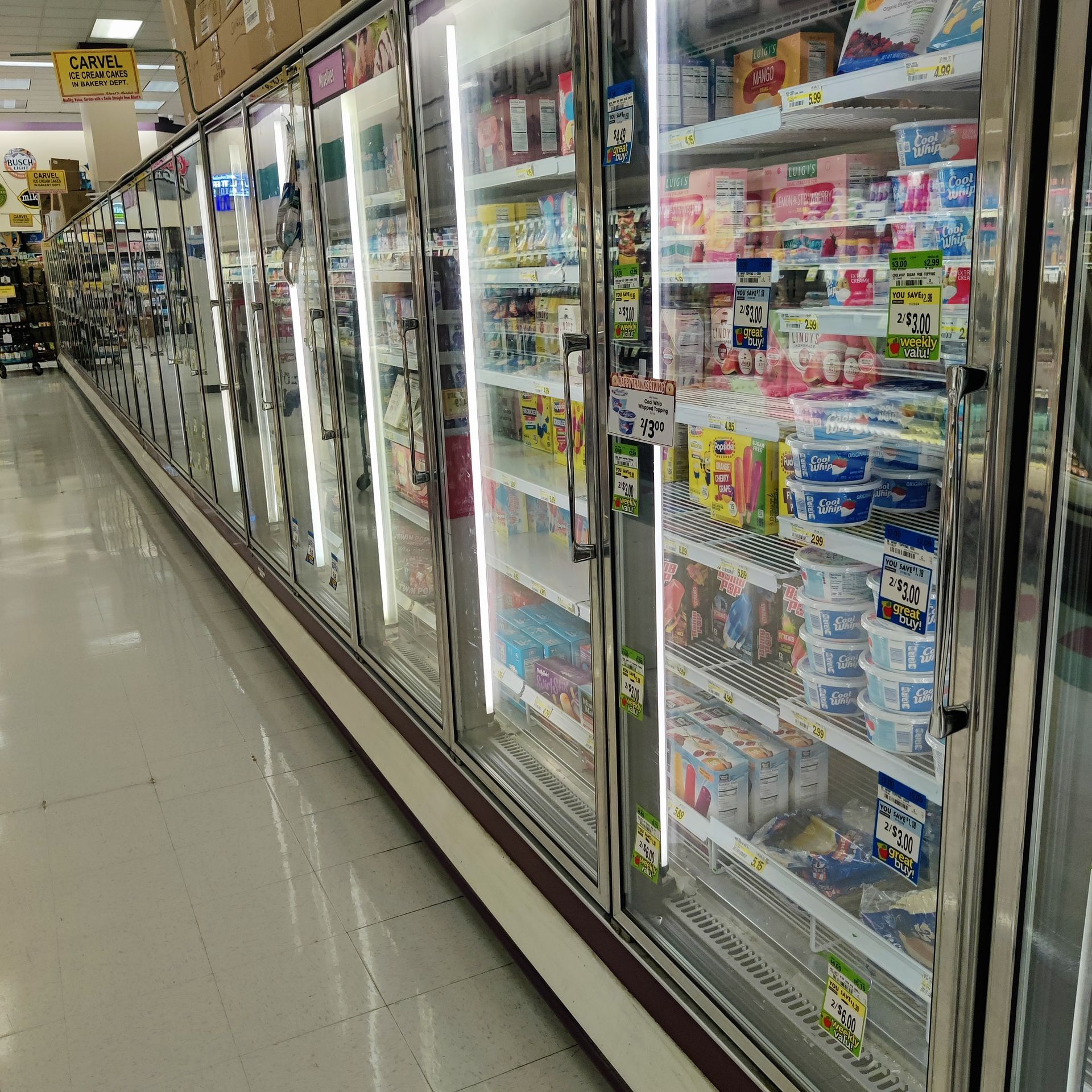 Grocery store freezer aisle with rows of glass-doored refrigerators stocked with frozen foods and ice cream.