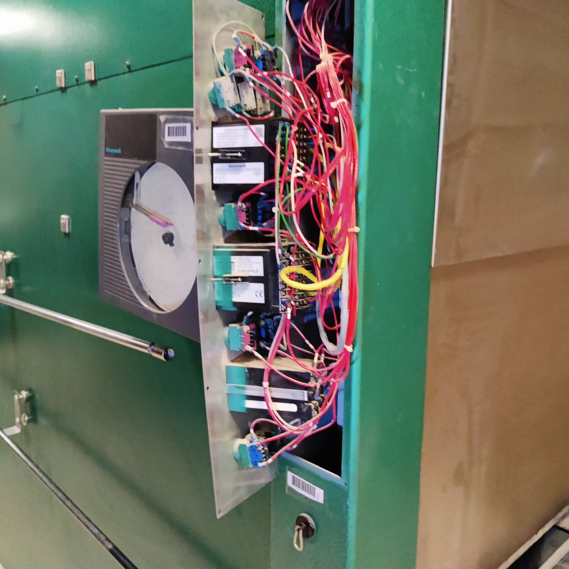 Open electrical panel with exposed multicolored wiring beside a green wall and fan unit