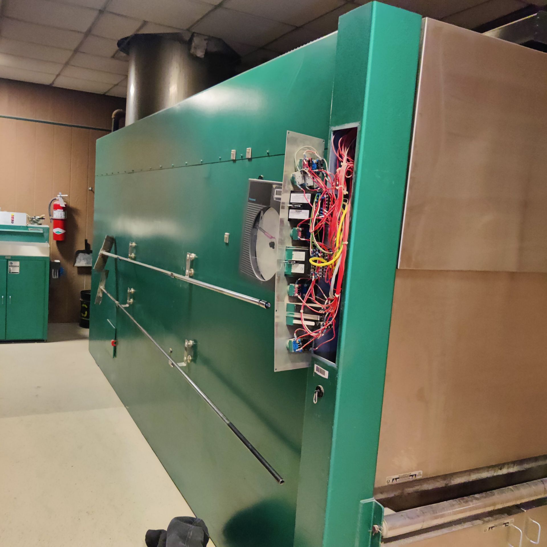 Large green industrial machine with an open side panel exposing wiring in a utility room