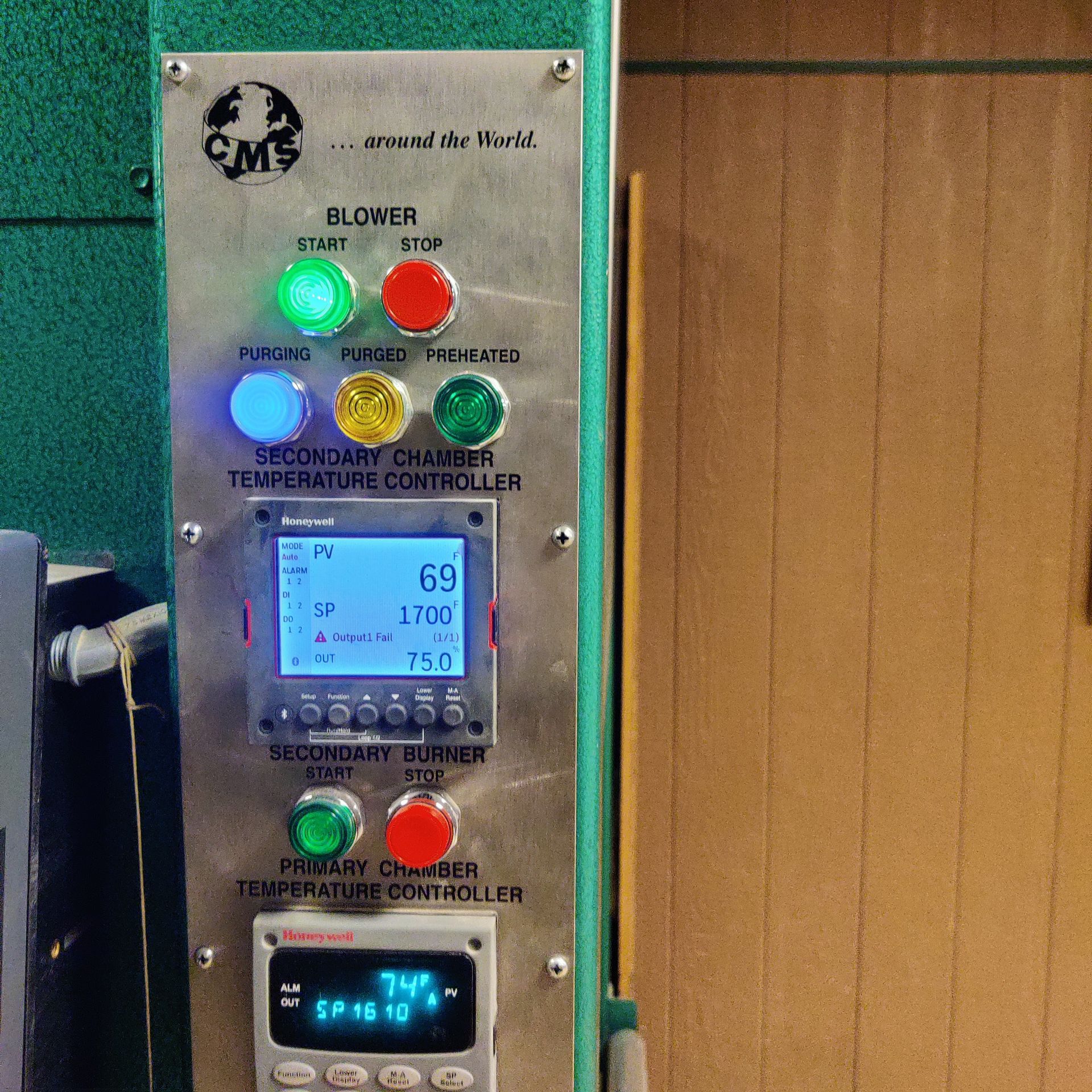 Close-up of a metal control panel with lit green, blue, and red indicators and a small digital display.