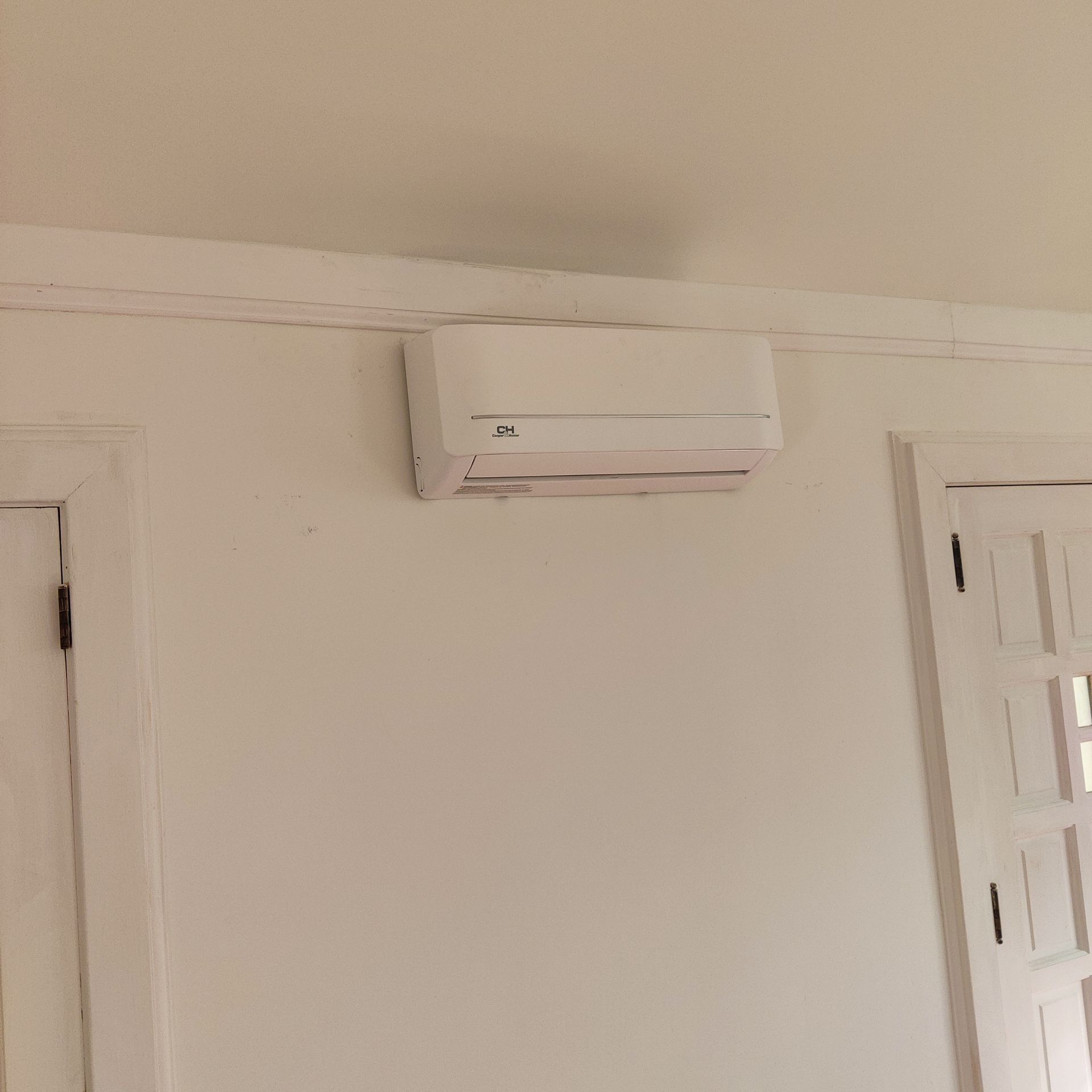 Wall-mounted white air conditioner on a beige wall beside a white doorway