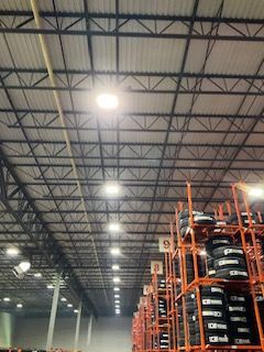 Warehouse interior with high metal ceiling lights and stacked pallets of tires on orange racks