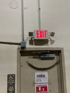 Red EXIT sign above a doorway with a wheelchair-accessible access plate on the left.