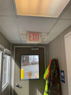 Hallway exit door with illuminated EXIT sign and reflective safety vest hanging beside it