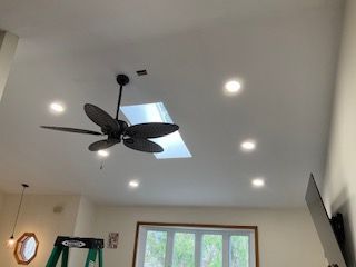 Ceiling fan and skylight in a bright living room with recessed lights and a window.