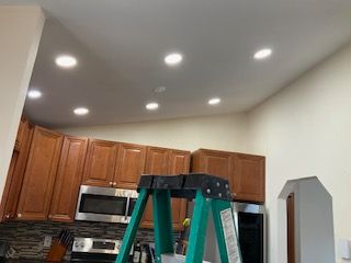 Kitchen ceiling with recessed lights and a green step ladder in front of wooden cabinets